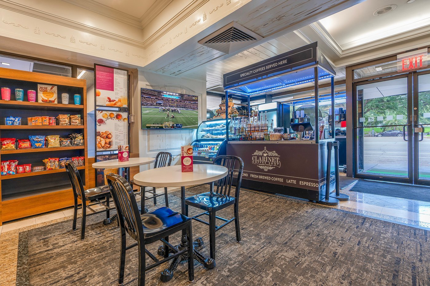 Coffee shop interior with tables, chairs, snack shelves, TV, and coffee counter.